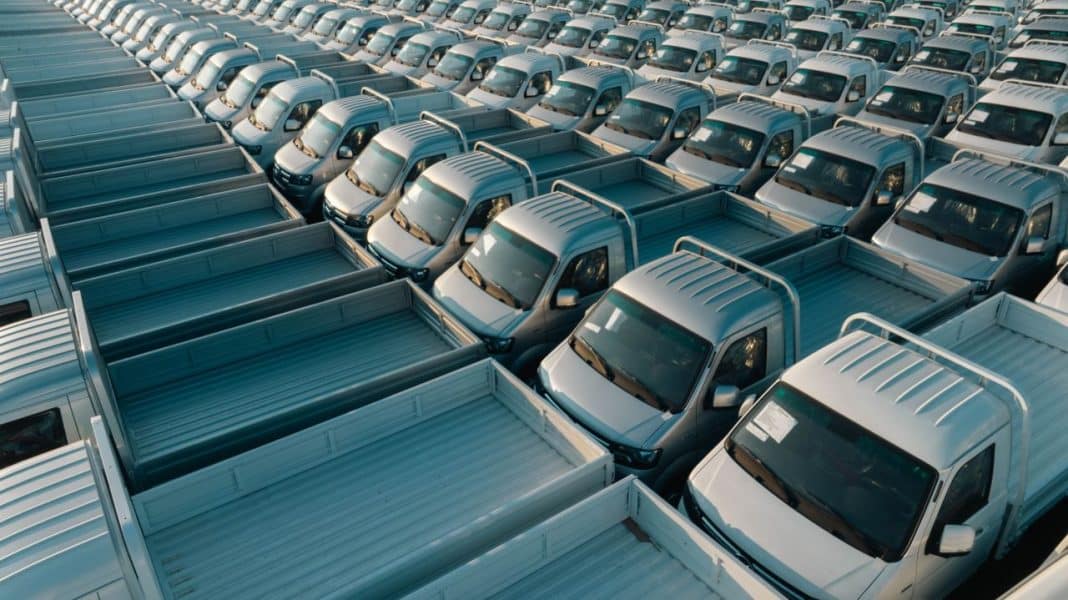Wielki parking z nowoczesnymi samochodami dostawczymi, ustawionymi w równych rzędach.
