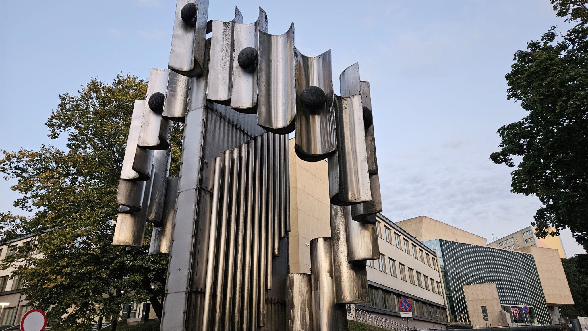 Metalowa rzeźba w centrum Olsztyna, stojąca obok szkoły muzycznej, z widocznymi uszkodzeniami konstrukcji.