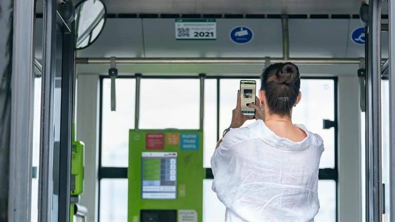 Kobieta skanuje kod QR na ekranie w autobusie w Olsztynie, widoczny jest zielony terminal biletowy.