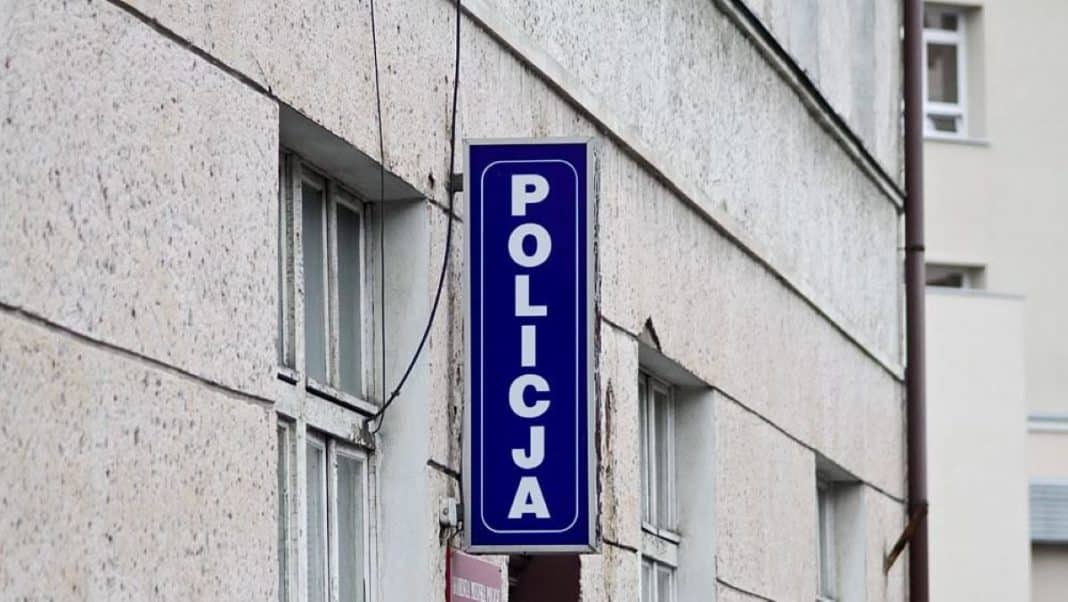 Zdjęcie budynku z widocznym niebieskim znakiem 'POLICJA' na ścianie.