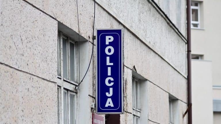 Zdjęcie budynku z widocznym niebieskim znakiem 'POLICJA' na ścianie.