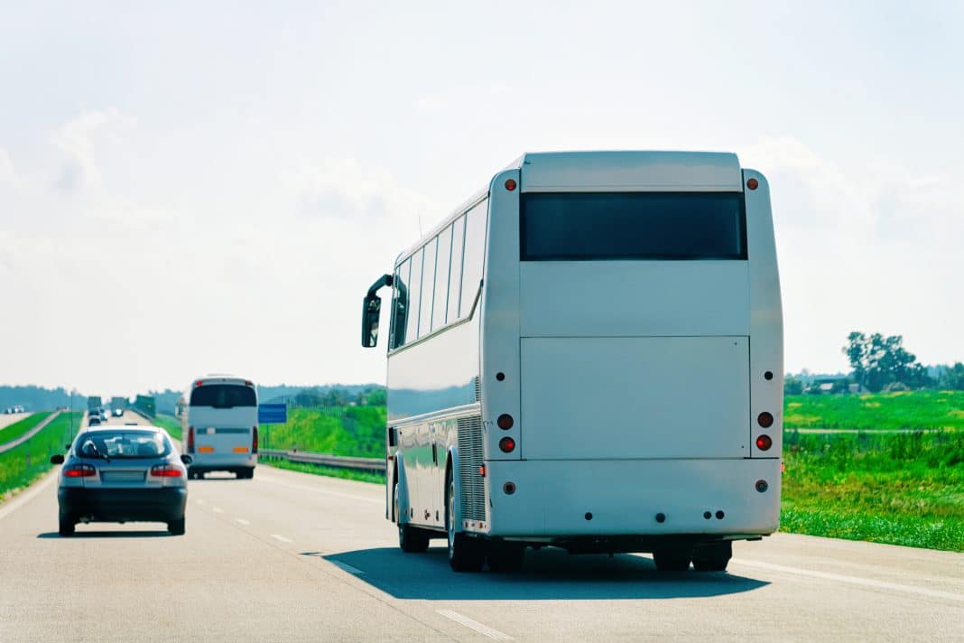 Autobus na drodze między miastami, w tle zielone pola i niebo z chmurami.