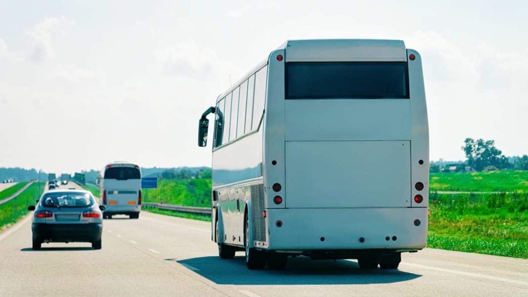 Autobus na drodze między polami, w tle inne pojazdy i krajobraz wiejski.