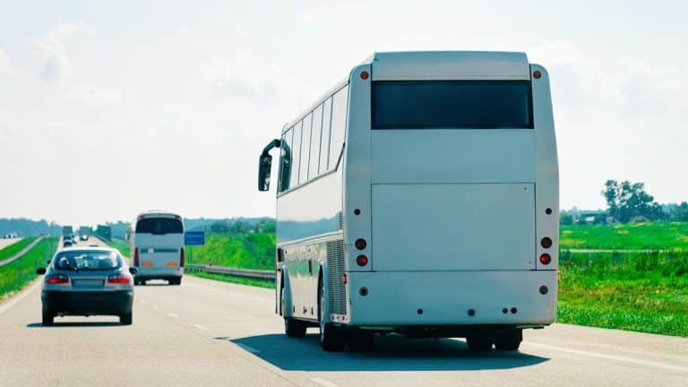 Autobus na drodze między polami, w tle inne pojazdy i krajobraz wiejski.