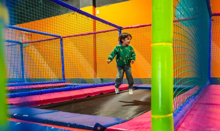 Dziecko bawi się na trampolinie w kolorowej sali zabaw.