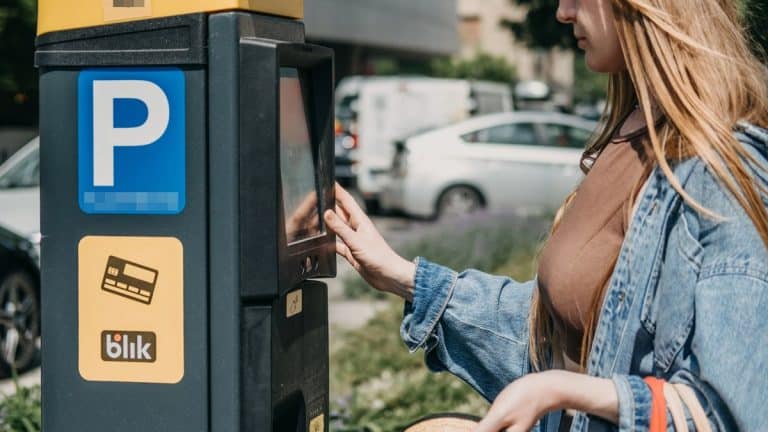 Kobieta korzysta z parkomatu w Olsztynie, w tle samochody na parkingu.