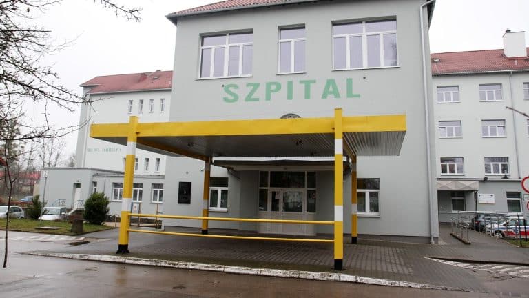 Szpital w Ostródzie, budynek z napisem 'SZPITAL' na fasadzie, wejście główne z daszkiem.