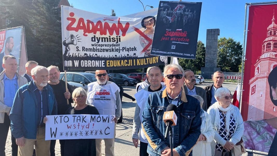 Grupa ludzi na protestie z transparentami i plakatami w centrum Olsztyna.