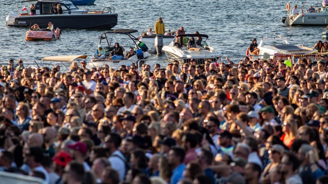 Tłum ludzi na brzegu jeziora podczas festiwalu w Olsztynie, w tle łodzie na wodzie.