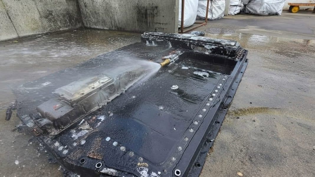 Wymontowana bateria samochodu elektrycznego podczas gaszenia pożaru, na zewnątrz, z widoczną wodną mgiełką.
