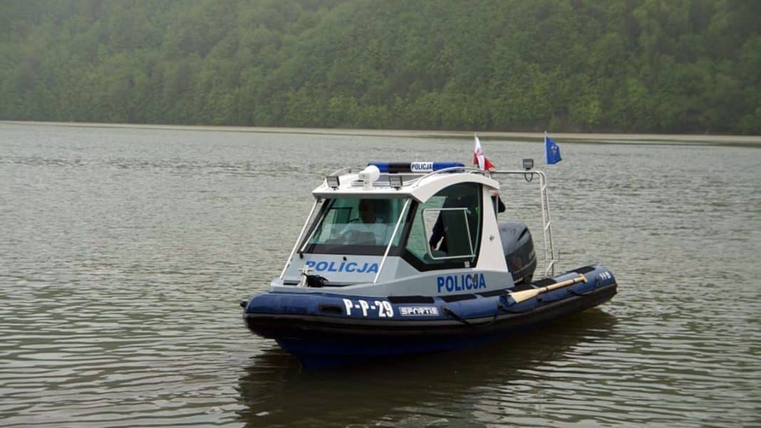 Patrol wodny na jeziorze Dadaj, policyjny ponton z flagami, w tle las.