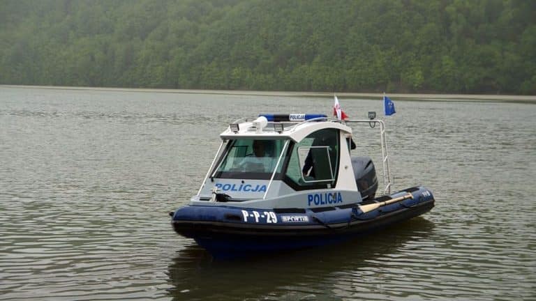 Patrol wodny na jeziorze Dadaj, policyjny ponton z flagami, w tle las.