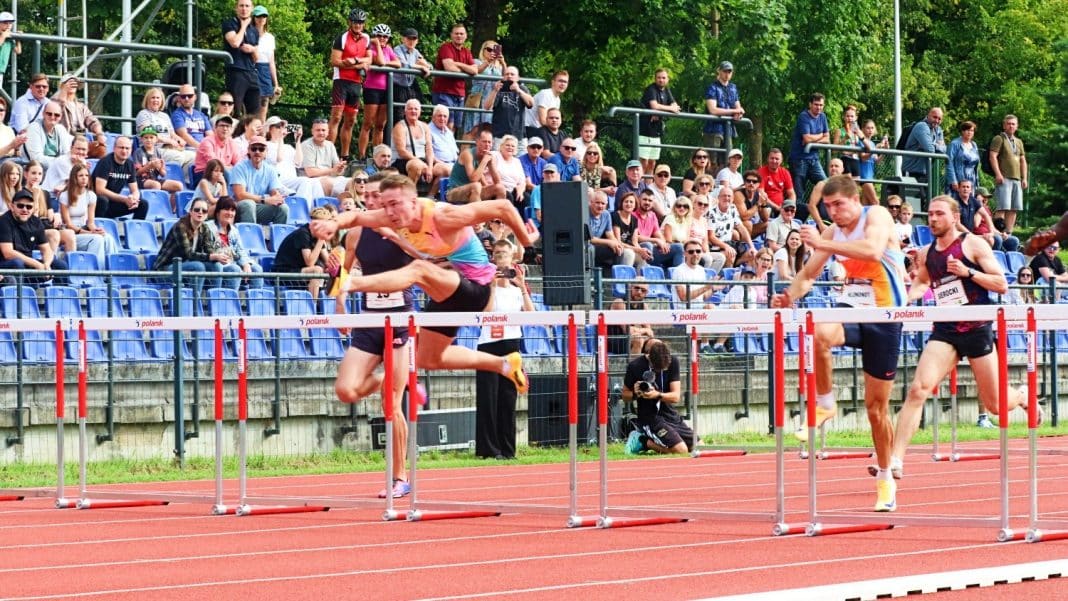 Biegacze podczas startu na stadionie lekkoatletycznym w Kortowie, z widownią i zielonym otoczeniem w tle.