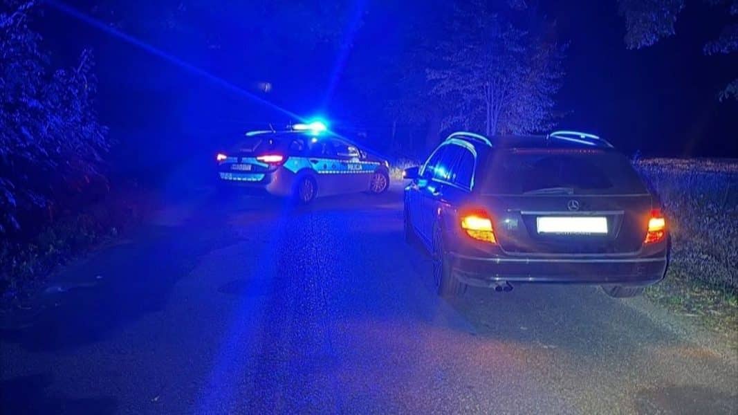 Policja na drodze powiatowej po wypadku, widoczne dwa samochody, jeden z nich to Mercedes.