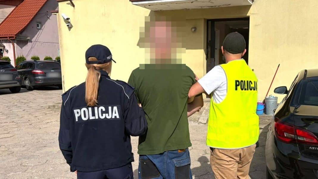 Mężczyzna zatrzymany przez policję na zewnątrz budynku, w tle samochody i budynek.
