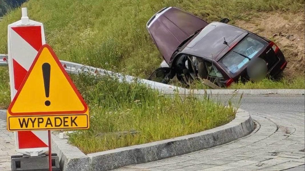 Samochód wypadł z ronda i zatrzymał się w rowie, obok znak ostrzegający o wypadku.