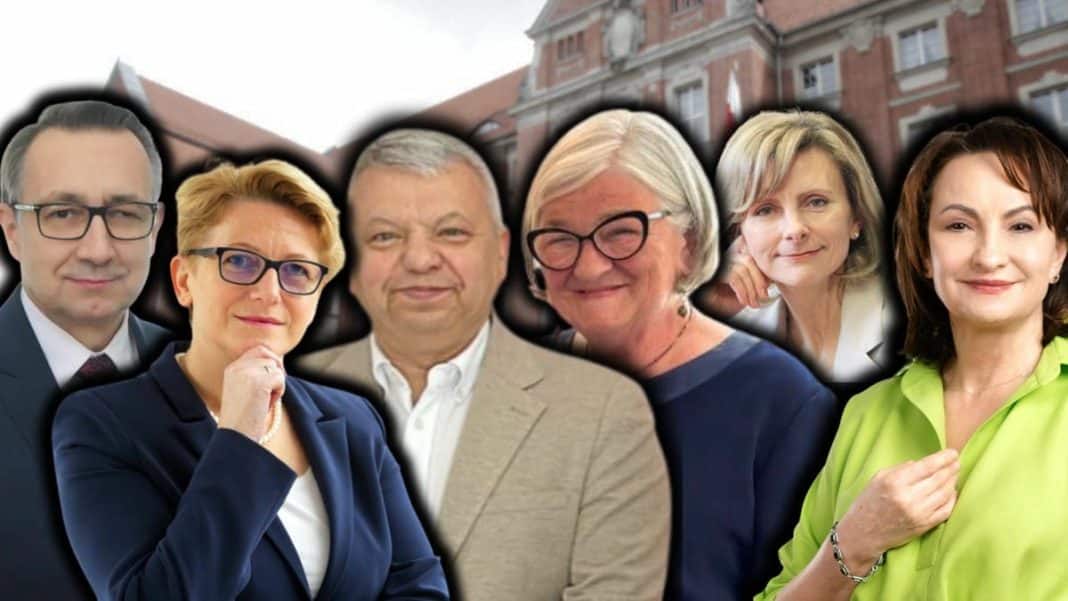 Grupa siedmiu osób na tle budynku, w tym kobiety i mężczyźni, w formalnych i casualowych strojach.