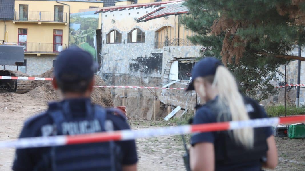 Widok na uszkodzoną ścianę hotelu podczas akcji ratunkowej, z policjantami w tle.