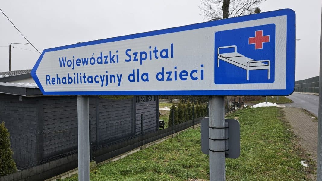 Tablica kierunkowa do szpitala rehabilitacyjnego dla dzieci na tle drogi i budynków.