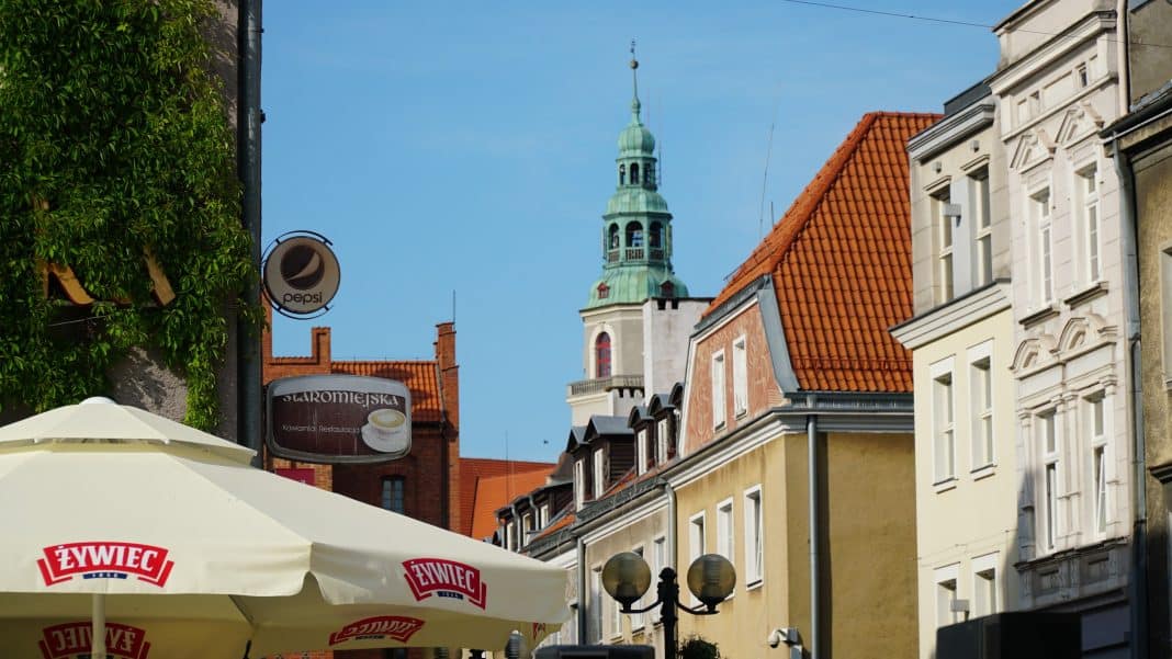 Widok na olsztyńską starówkę z budynkami i wieżą kościoła w tle, na pierwszym planie parasol z logo Żywiec.