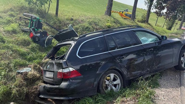 Uszkodzony czarny samochód po wypadku na poboczu drogi, na miejscu lądował śmigłowiec ratunkowy.