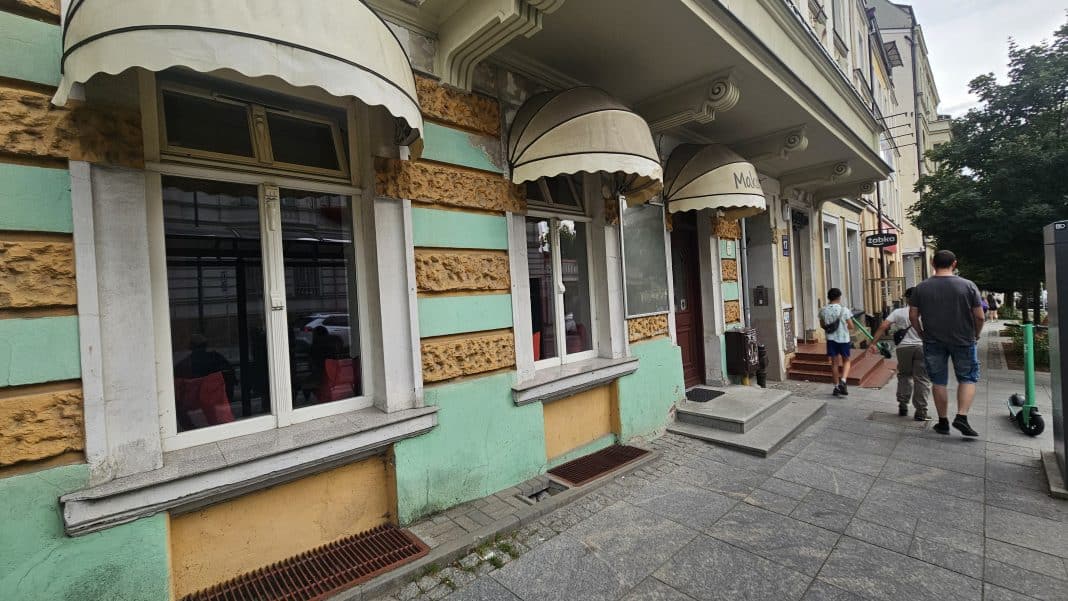 Widok na zamknięty lokal gastronomiczny przy ul. Pieniężnego 17 w centrum Olsztyna, z wejściem i oknami, wokół chodnik i przechodnie.