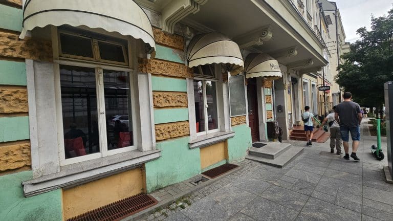 Widok na zamknięty lokal gastronomiczny przy ul. Pieniężnego 17 w centrum Olsztyna, z wejściem i oknami, wokół chodnik i przechodnie.