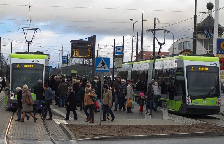 Tłum pasażerów czekających na przystanku tramwajowym w Olsztynie, obok nowoczesnych tramwajów.