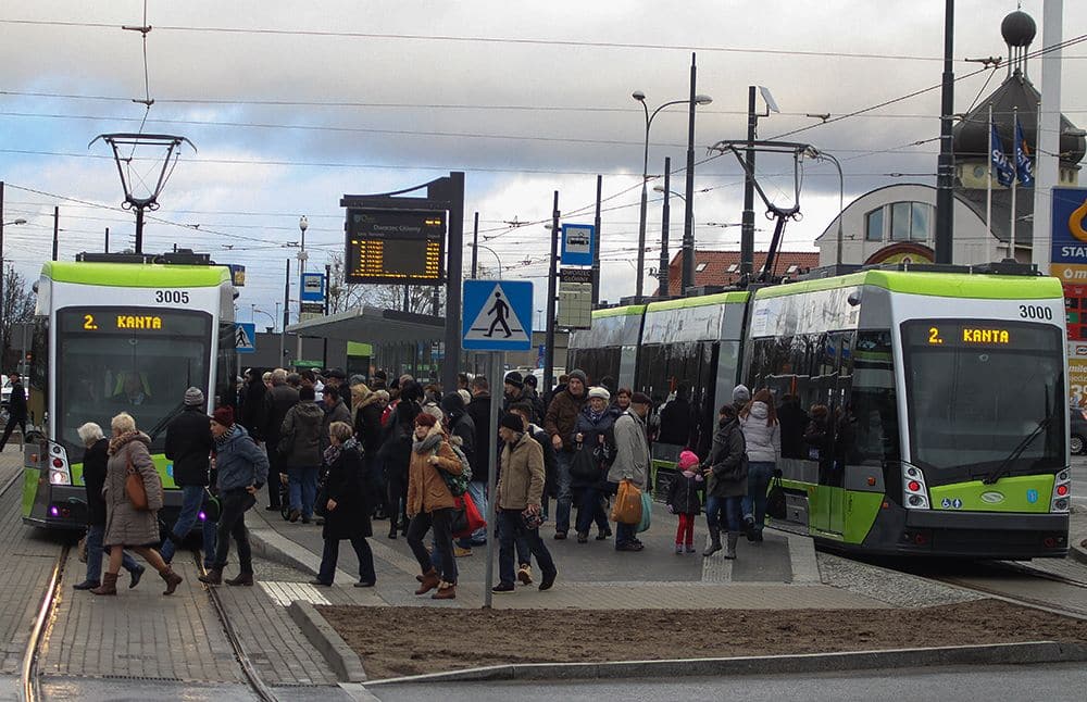 Tłum pasażerów czekających na przystanku tramwajowym w Olsztynie, obok nowoczesnych tramwajów.