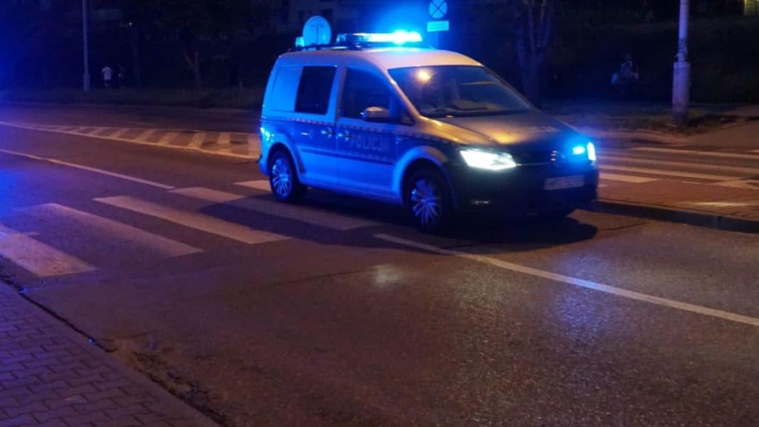 Samochód policyjny z włączonymi światłami na ulicy w nocy, na pasach dla pieszych.
