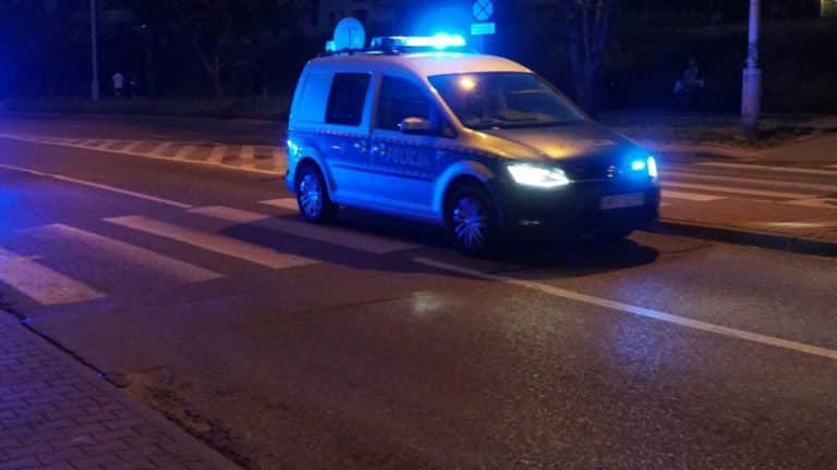 Samochód policyjny z włączonymi światłami na ulicy w nocy, na pasach dla pieszych.