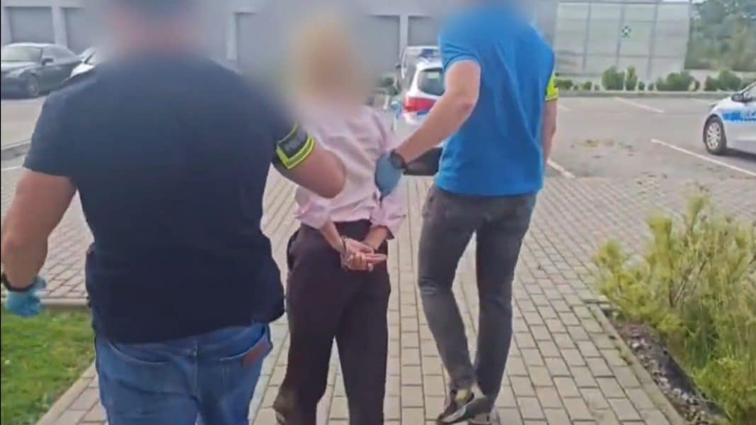 Policjanci zatrzymują kobietę na parkingu, w tle samochody i budynek.