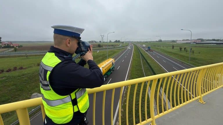 Policjant na moście nad trasą S7 robi zdjęcia pojazdów na drodze.