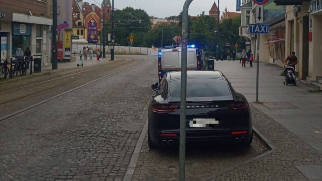 Czarne Porsche zaparkowane przy ulicy 11 Listopada w centrum Olsztyna, z blokadą na kole.