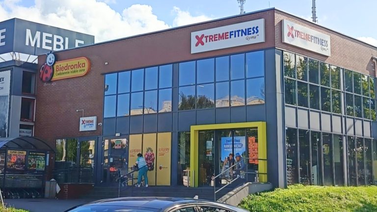 Nowoczesna siłownia Xtreme Fitness w Olsztynie przy ul. Pstrowskiego 26, widoczna z zewnątrz, z dużymi oknami i logo.