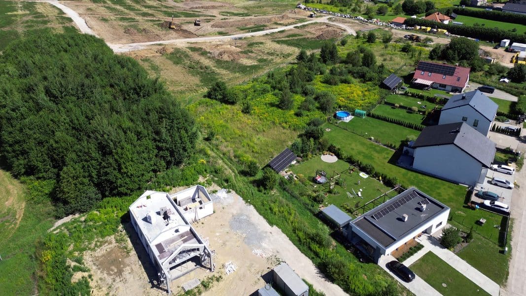 Widok na teren pod budowę osiedla z domami i ciężkim sprzętem na początku inwestycji.