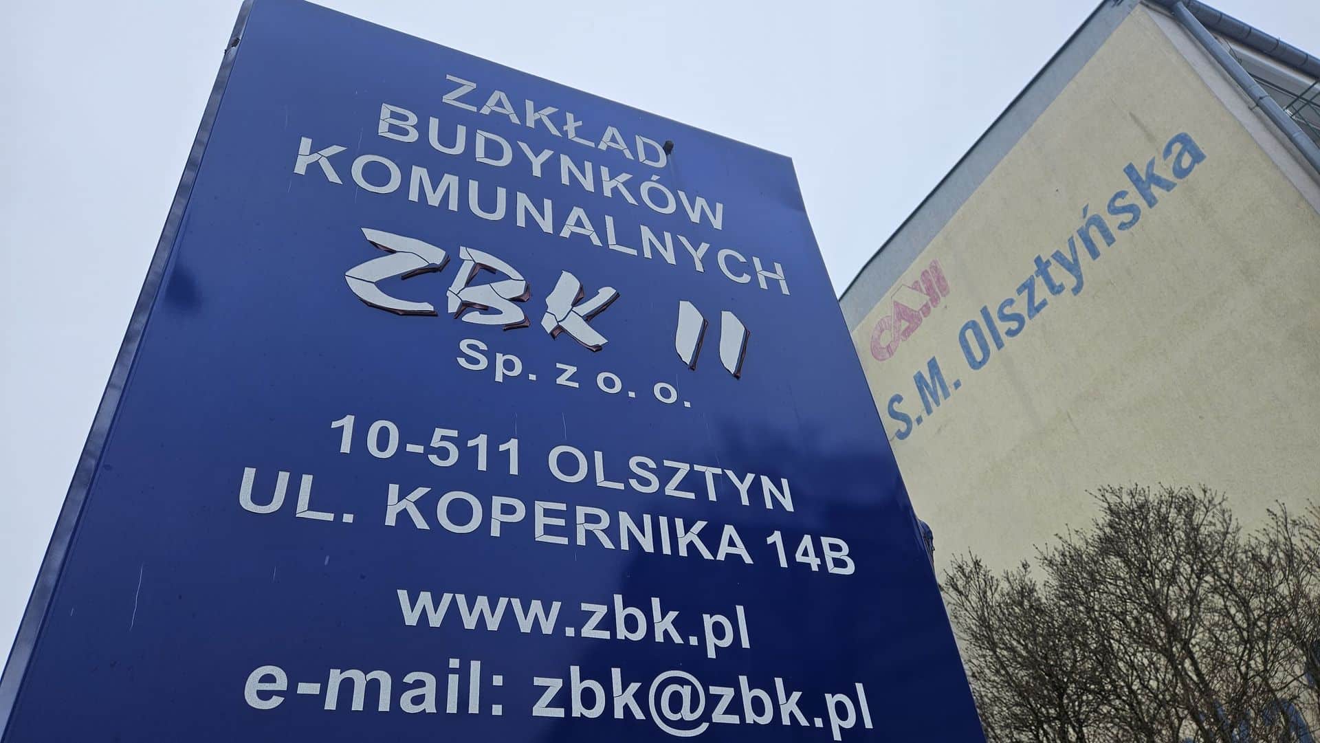 Tablica informacyjna Zakładu Budynków Komunalnych w Olsztynie, z widocznymi danymi kontaktowymi i adresem.