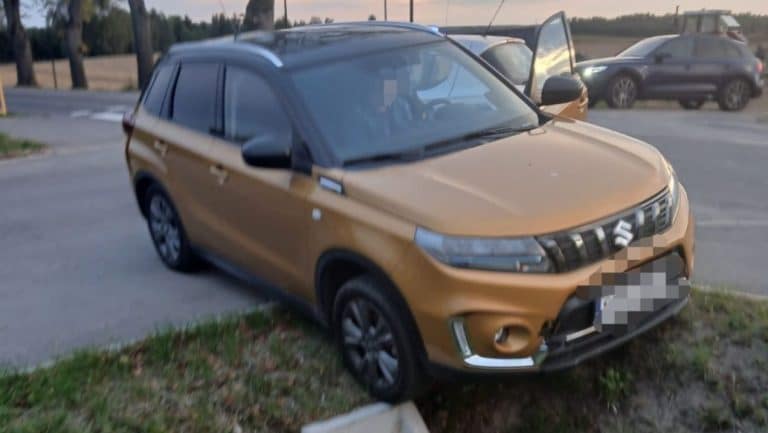 Dachowany samochód marki Suzuki na poboczu drogi krajowej nr 16, obok leży odłamany element pojazdu.