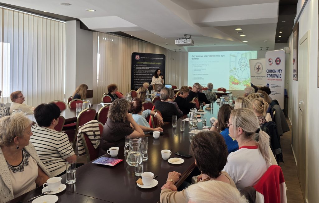 Spotkanie seniorów w sali konferencyjnej, prezentacja na ekranie o zdrowym odżywianiu.