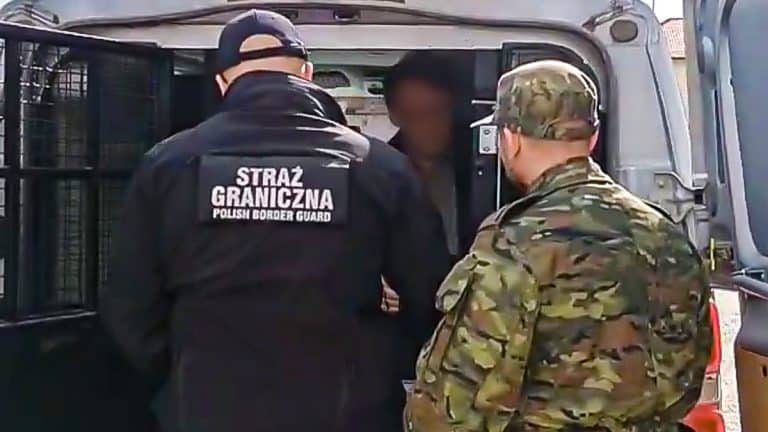 Policjant i strażnik graniczny zatrzymują mężczyznę w samochodzie na granicy Polski i Rosji.