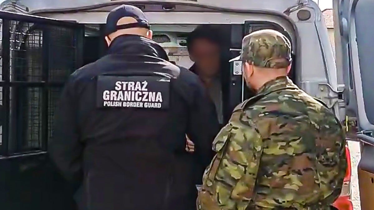 Policjant i strażnik graniczny zatrzymują mężczyznę w samochodzie na granicy Polski i Rosji.