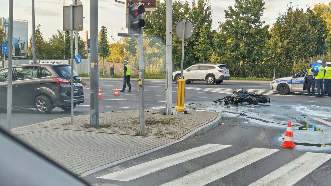 Rozbity motocykl na skrzyżowaniu, policja i funkcjonariusze na miejscu wypadku.
