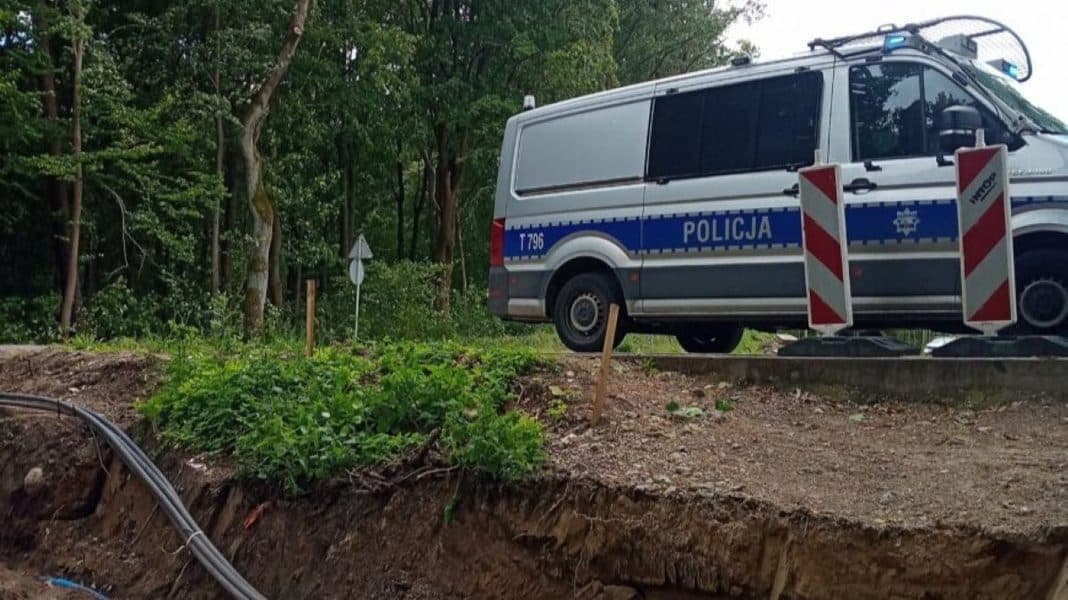 Na zdjęciu teren budowy z policyjnym samochodem na tle drzew, barierkami i wykopem.