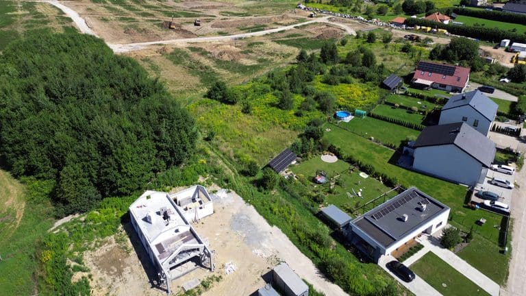Widok na teren pod budowę osiedla z domami i ciężkim sprzętem na początku inwestycji.