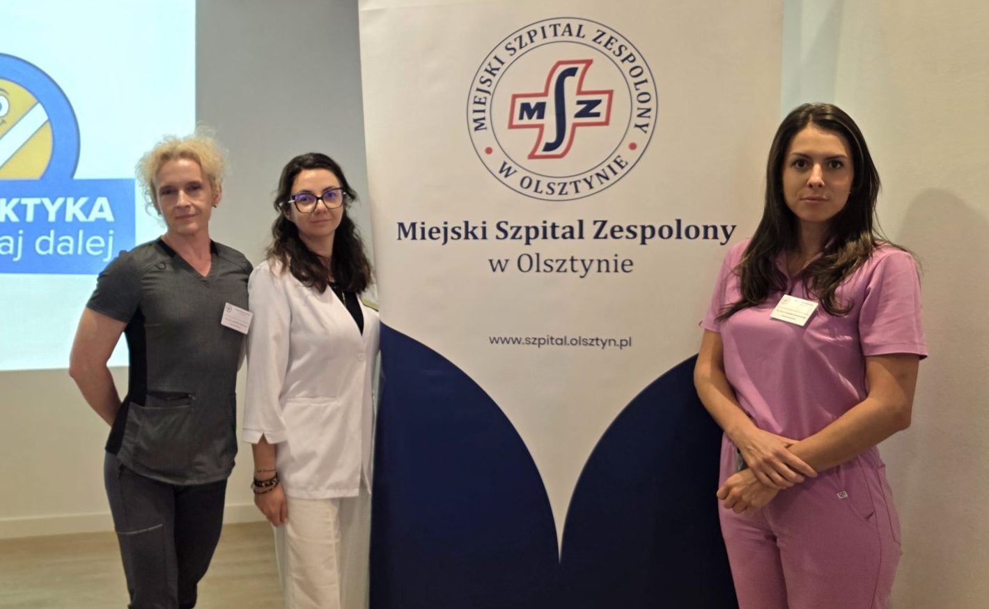 Trzy kobiety stoją obok banerów podczas wydarzenia zdrowotnego dla seniorów w Olsztynie.