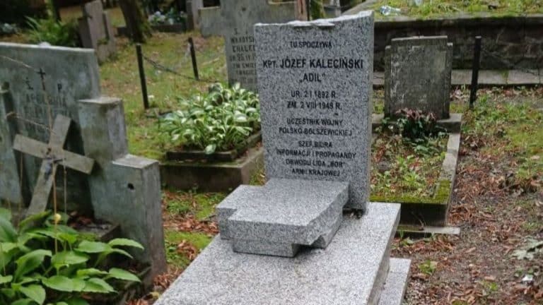 Zniszczony nagrobek na cmentarzu w Giżycku, widoczny pomnik z inskrypcją o żołnierzu wojny polsko-bolszewickiej.