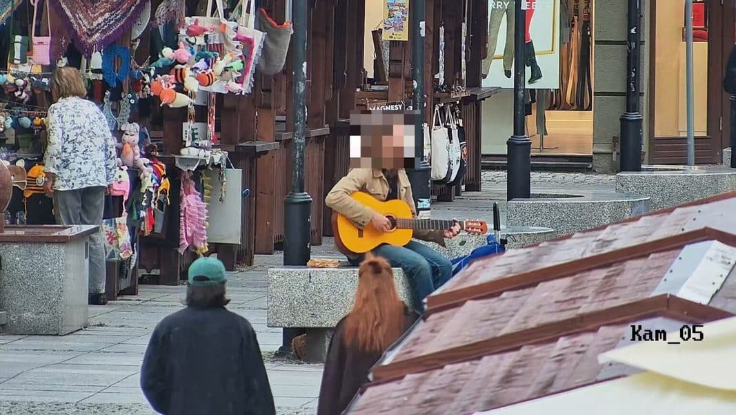 Mężczyzna grający na gitarze na olsztyńskiej starówce, w tle stragany z zabawkami i innymi przedmiotami.