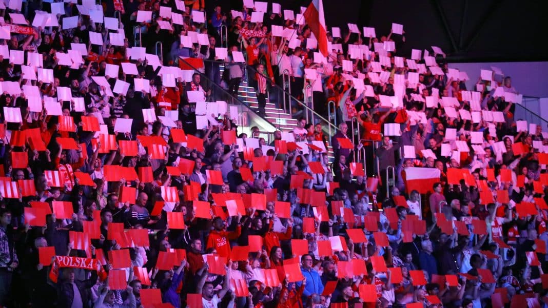 Tłum kibiców w hali Urania, trzymających czerwono-białe kartki i flagi, wspierających reprezentację Polski.