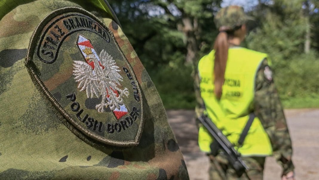 Funkcjonariusz Straży Granicznej w kamuflażu, w tle patrolowa kobieta w odblaskowej kamizelce, na tle zieleni.