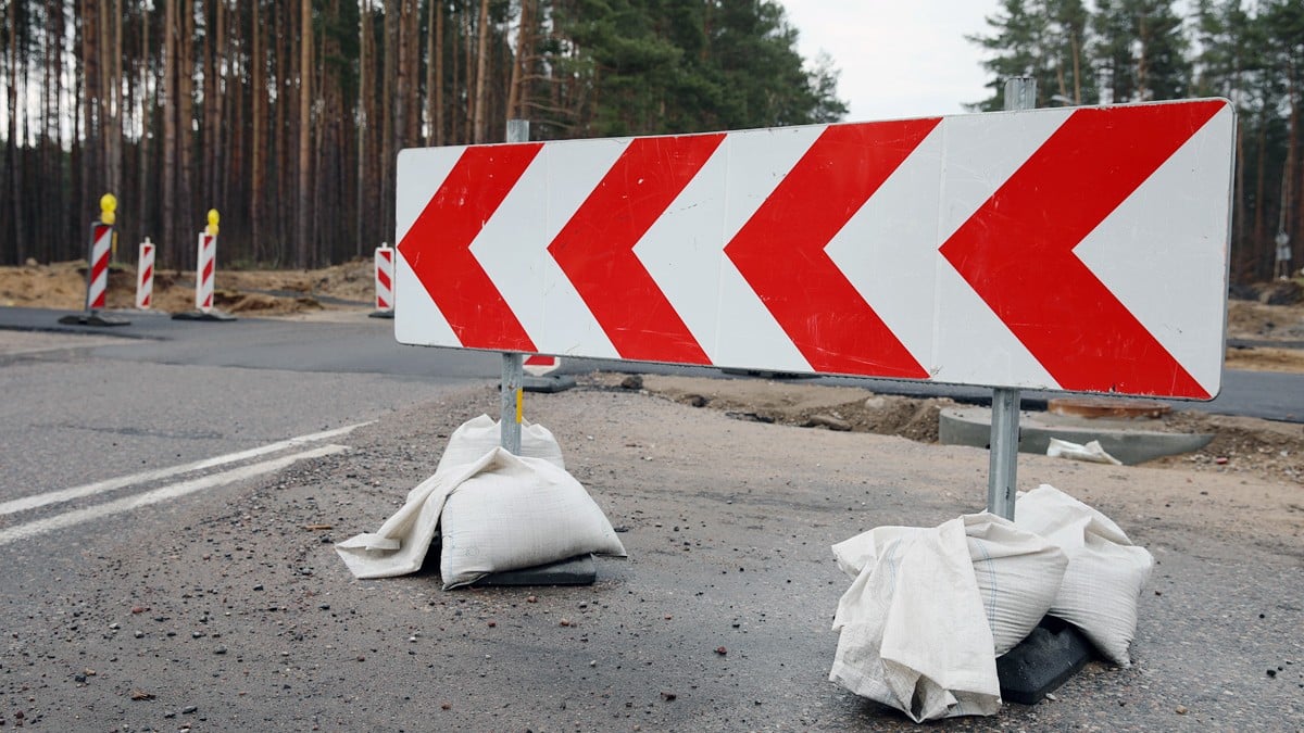 Bariera drogowa z czerwono-białymi pasami na zamkniętej ulicy w trakcie prac remontowych, otoczona workami z piaskiem.